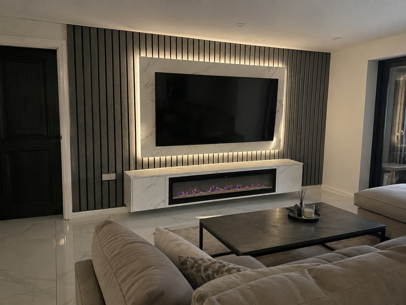 A charcoal slat media wall with a backlit marble TV surround and a linear fire